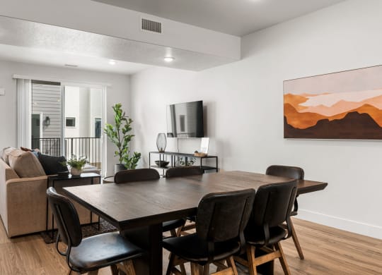 a dining room table with chairs and a couch in a room with white walls and hardwood
