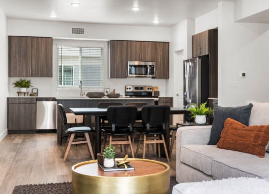 a living room with a couch a table and chairs and a kitchen with a refrigerator and microwave