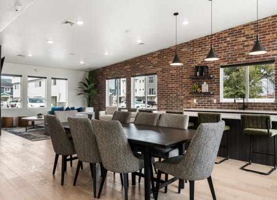 a dining area with a long table and chairs and a brick wall with windows in the background