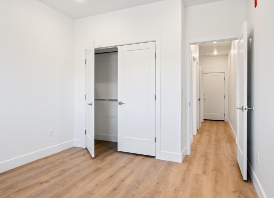 a bedroom with white walls and wood floors and a closet