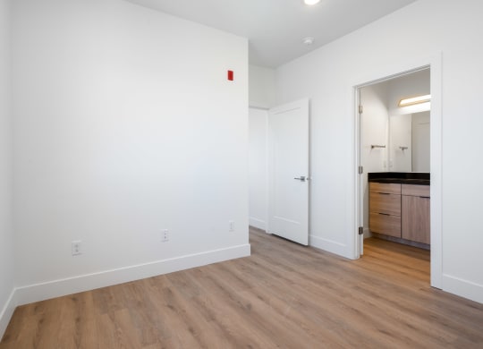 a bedroom with white walls and wood flooring and a door to a bathroom