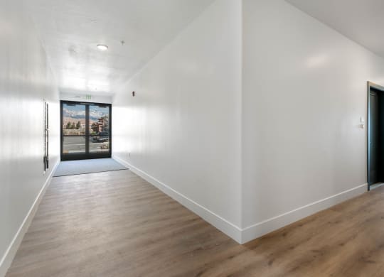 a hallway with white walls and wood floors and a black door