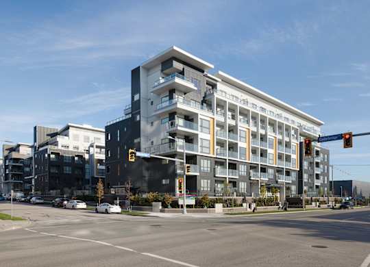 A modern multi-story building with balconies is situated on a street corner with traffic lights.