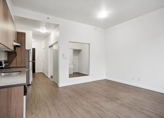 an empty living room and kitchen with white walls and wood flooring