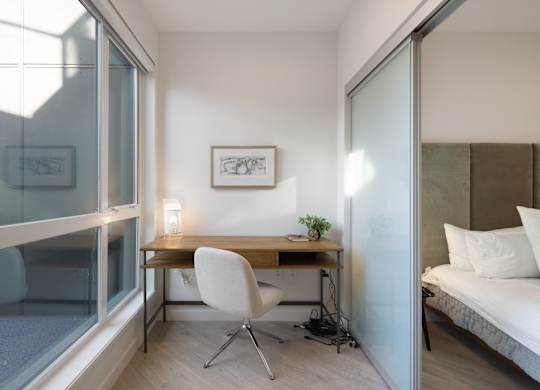 A white chair is in front of a desk with a laptop and a plant on it.