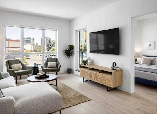 A modern living room with a large window, a sofa, a coffee table, a TV, and a bed.