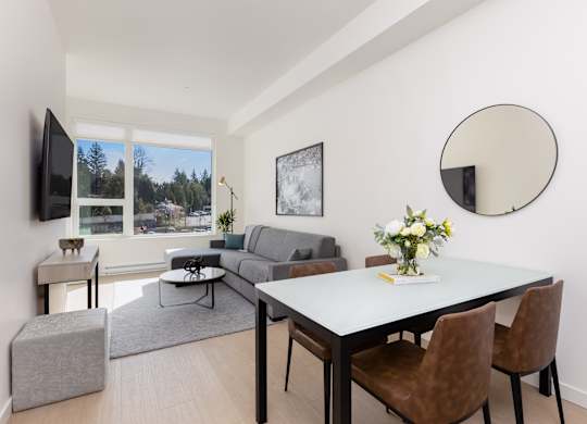 A modern living room with a grey sofa, a white dining table, and a television.
