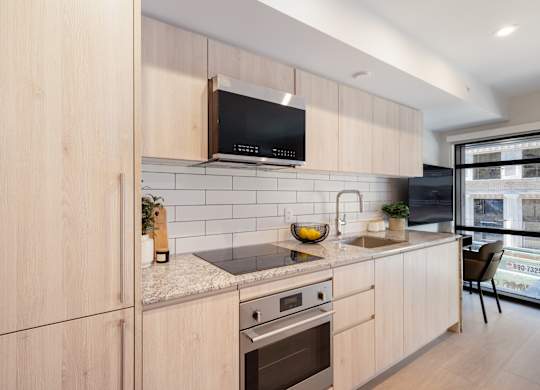 A modern kitchen with wooden cabinets and a black microwave above the stove.