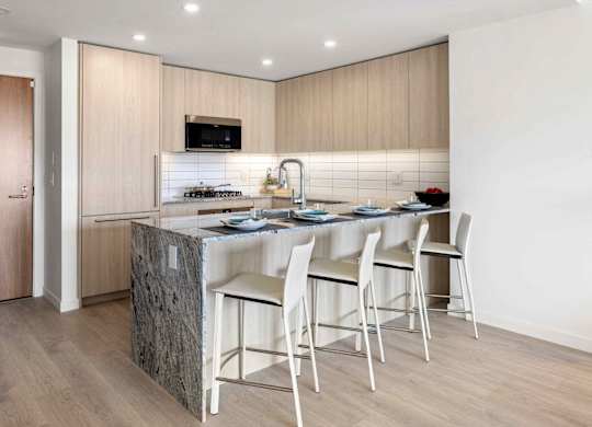 A kitchen with a granite island and white chairs.