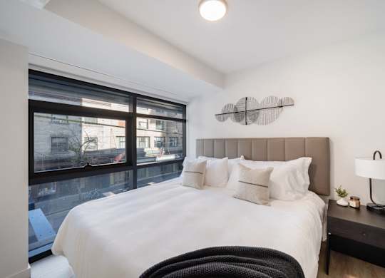 A bedroom with a large bed and a window overlooking a cityscape.