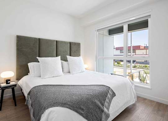 A bedroom with a large bed and a window overlooking a balcony.