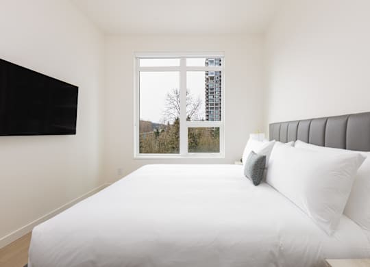 A white bed with a grey headboard and two pillows in a room with a window.