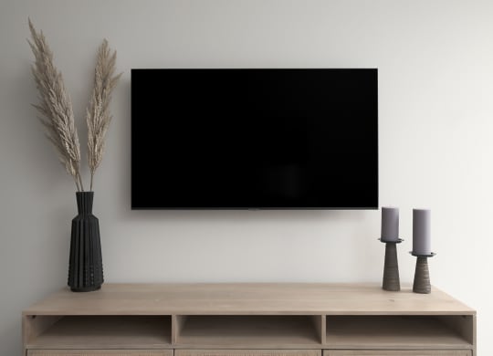 a television on the wall above a wooden shelf with a vase and two lamps