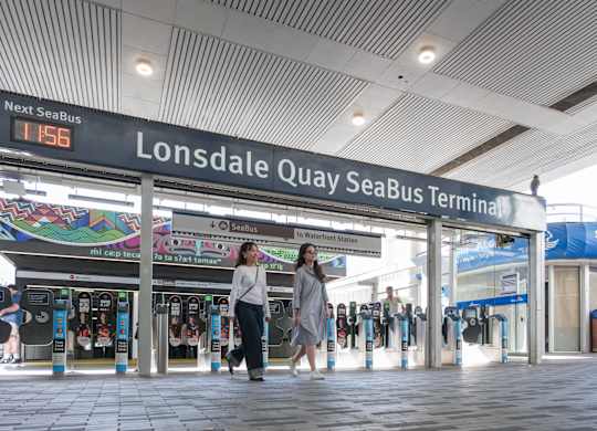 Two women walking in a station with a sign that says Lonsdale Quay SeaBus.