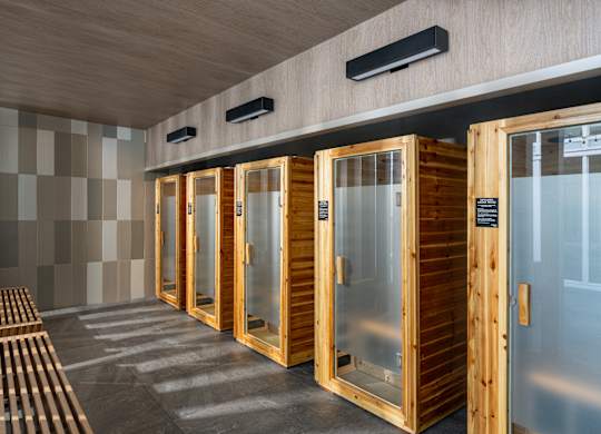 A row of wooden saunas with glass doors are lined up in a room.