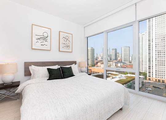 A bedroom with a large bed and a city view through the window.