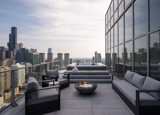 A modern balcony with a fire pit and seating area overlooking a city skyline.