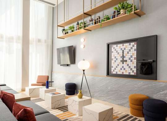 A modern living room with a grey sofa, a wooden shelf with plants, and a black and white tiled wall.