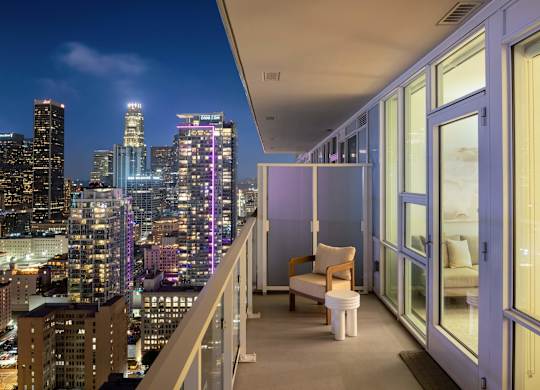 A balcony with a chair and a table overlooking a city skyline at night.