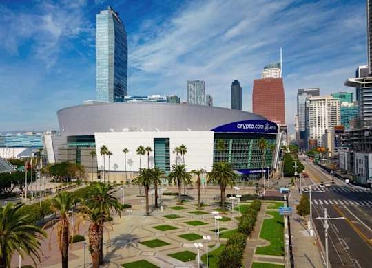 A modern building with a glass facade is surrounded by palm trees and other greenery.