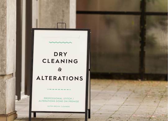 A sign that says dry cleaning and alterations is propped up against a wall.