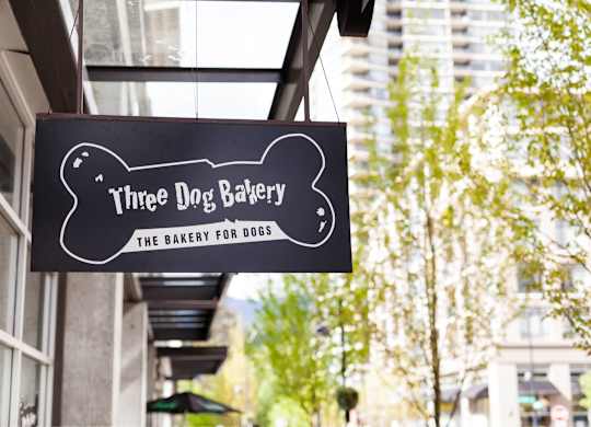 A black and white sign for Three Dog Bakery hangs from a building.