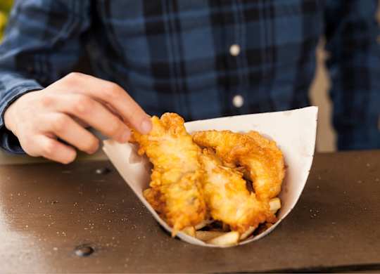 A person in a plaid shirt is holding a paper cone filled with fried food.