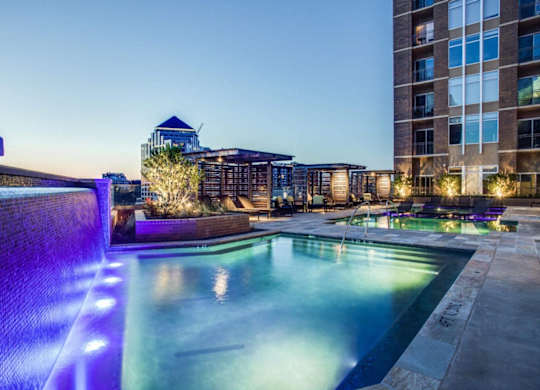 A pool with a waterfall and lights in the background.