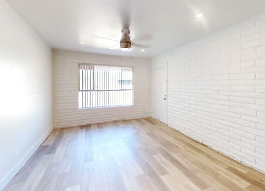 A room with a white ceiling, a window with blinds, and a wooden floor.