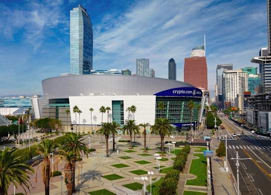 A modern building with a glass facade is surrounded by palm trees and other greenery.