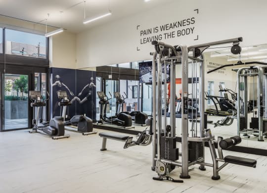 a gym with weights and cardio machines and a sign that reads pain is weakness leaving