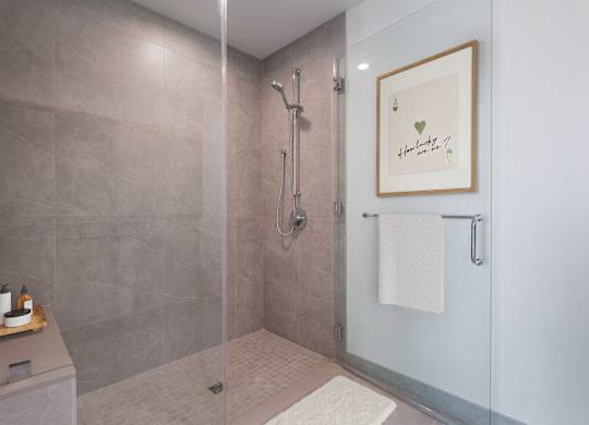 A bathroom with a glass shower stall and a towel rack with a heart-shaped picture hanging on the wall.