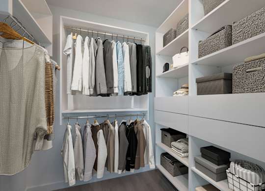 A white closet with clothes hanging and baskets on shelves.