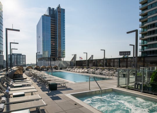 an outdoor pool with chaise lounge chairs and a city skyline in the background