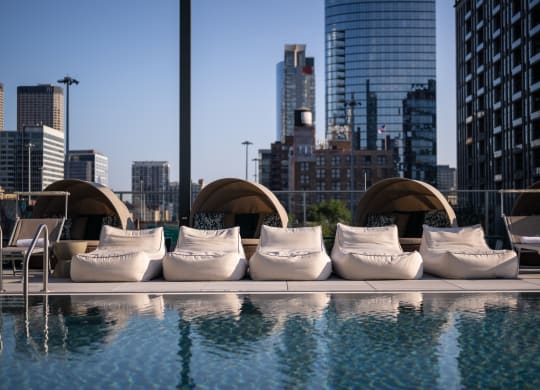 an outdoor pool with white lounge chairs and a city skyline in the background