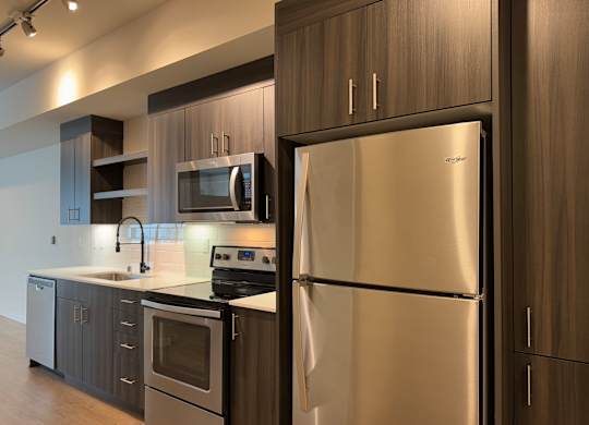 A modern kitchen with a stainless steel refrigerator and wooden cabinets at B Flats Apartments, Bremerton, 98337