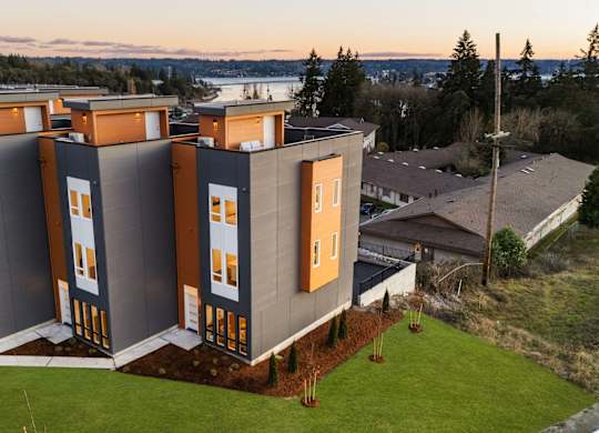 A modern building with grey and orange panels is surrounded by a green lawn. at The Narrows at Clare Apartments , Bremerton, Washington