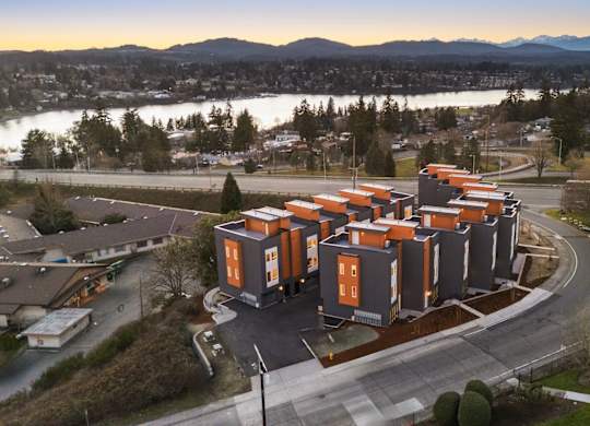 A modern building with orange and grey exterior is surrounded by a parking lot and a body of water in the background. at The Narrows at Clare Apartments , Bremerton, 98310
