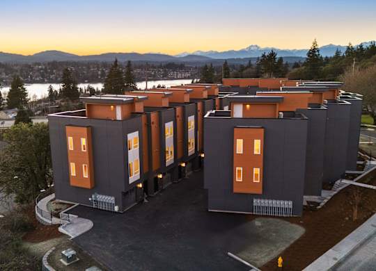 A modern building with orange windows is surrounded by a parking lot and trees. at The Narrows at Clare Apartments , Bremerton