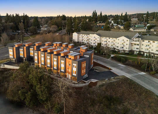 A large building with orange and white exterior is surrounded by trees and other buildings. at The Narrows at Clare Apartments , Washington