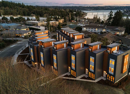 A series of modern buildings with orange and black accents are situated on a grassy area. at The Narrows at Clare Apartments , Bremerton, 98310