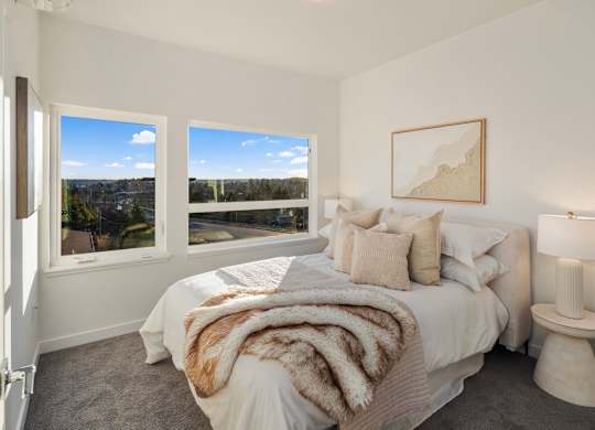A bedroom with a large bed and a view of the city through the window at The Narrows at Clare Apartments , Bremerton