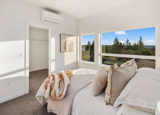 A bedroom with a large bed and a view of trees outside the window. at The Narrows at Clare Apartments , Bremerton, Washington