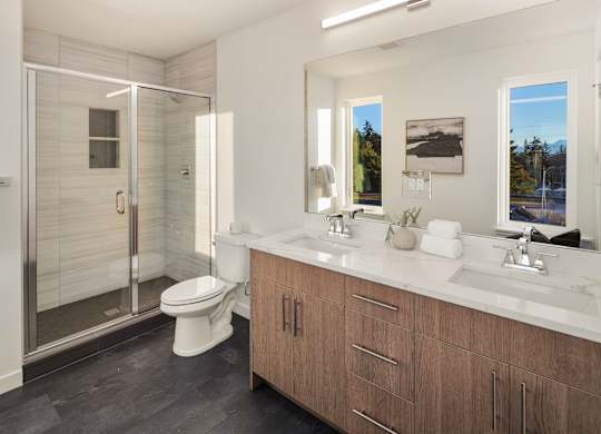 A bathroom with a walk-in shower, toilet, and double sinks. at The Narrows at Clare Apartments , Apartments, Bremerton, WA