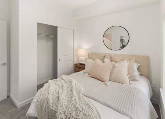 A bedroom with a bed, pillows, and a round mirror on the wall at The Narrows at Clare Apartments , Bremerton, 98310
