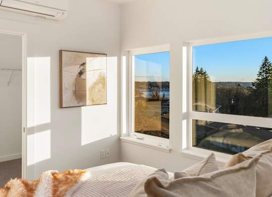 A bedroom with a large bed and a view of the outdoors through the windows at The Narrows at Clare Apartments , Apartments, Bremerton, WA