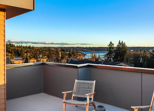 Two chairs are on a balcony overlooking a body of water and trees at The Narrows at Clare Apartments , Bremerton