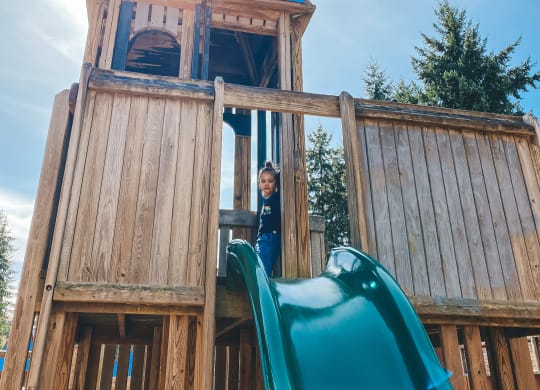 a young boy stands in the doorway of a wooden playset with a slide at Rivulet, Silverdale, 98383