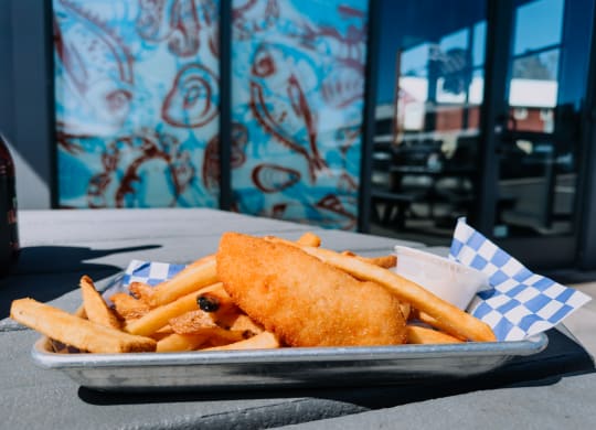 a plate of fish and chips on a table with graffiti in the background at Rivulet, Silverdale