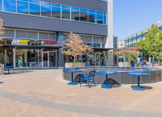 A Subway restaurant is located in a plaza with tables and chairs.